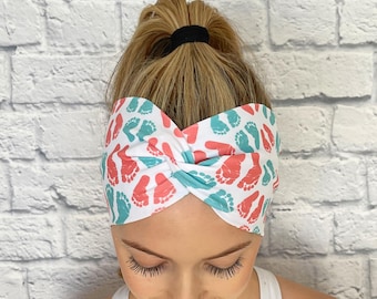 May include: A white headband with a twisted design features a pattern of pink and teal footprints.