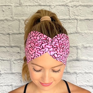 May include: A pink headband with a brain pattern. The headband is twisted and knotted at the top.