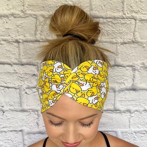 May include: A yellow and white headband with a pattern of cartoon ducks. The headband is twisted and worn on a person's head.