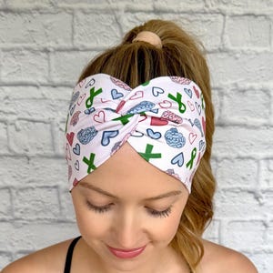 Woman with hair in curly ponytail wearing wide, twisted headband with green ribbon, pink and blue brain, and pink and blue heart print.