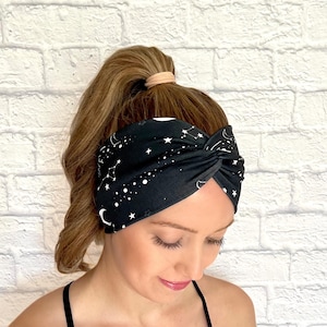 Woman with hair in curled ponytail wearing wide, twisted headband in black with white galaxy theme print.