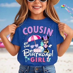 May include: A blue t-shirt featuring the text "COUSIN OF THE BIRTHDAY GIRL!" and a Minnie Mouse design. The graphic includes a pink parasol, sunglasses, a boombox, and a drink. The shirt is worn by a person.