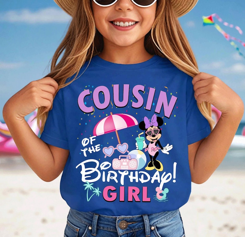 May include: A blue t-shirt featuring the text "COUSIN OF THE BIRTHDAY GIRL!" and a Minnie Mouse design. The graphic includes a pink parasol, sunglasses, a boombox, and a drink. The shirt is worn by a person.