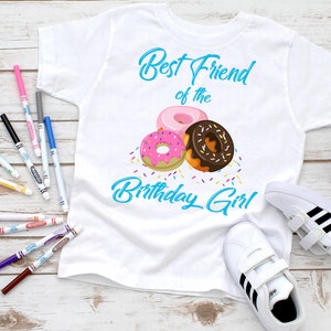 May include: White t-shirt with the text "Best Friend of the Birthday Girl" in blue script. The shirt features a graphic of three colorful donuts with sprinkles.