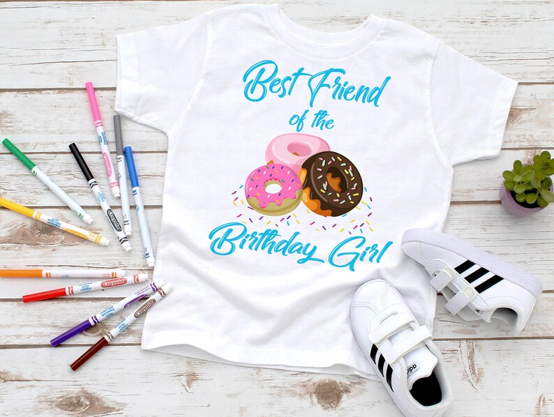 May include: White t-shirt with the text "Best Friend of the Birthday Girl" in blue script. The shirt features a graphic of three colorful donuts with sprinkles.