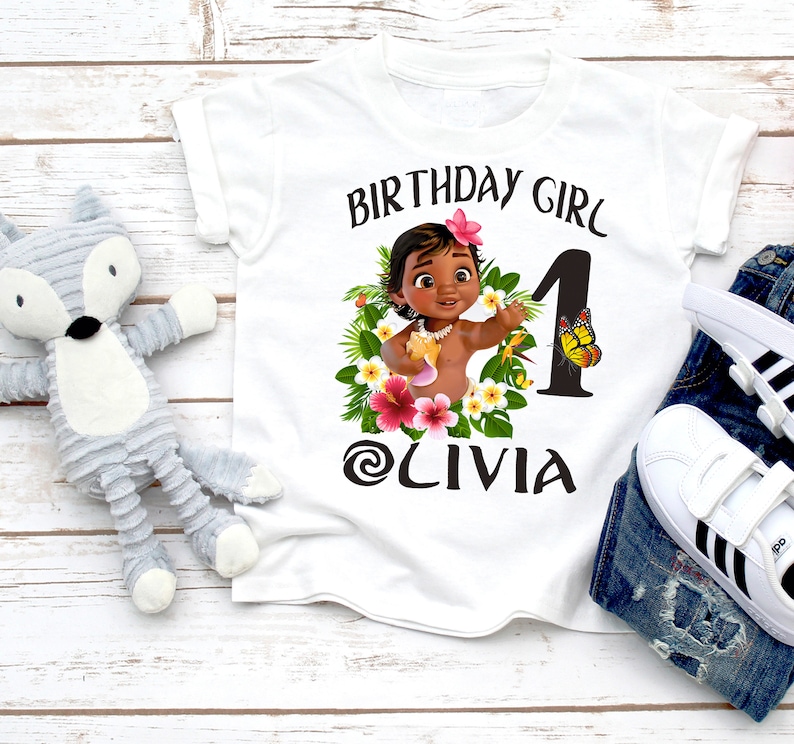 Pode incluir: Camiseta branca com um gr&aacute;fico de uma menina de desenho animado com flores e uma borboleta. O texto "Birthday Girl" e "Olivia" est&aacute; impresso na camiseta.