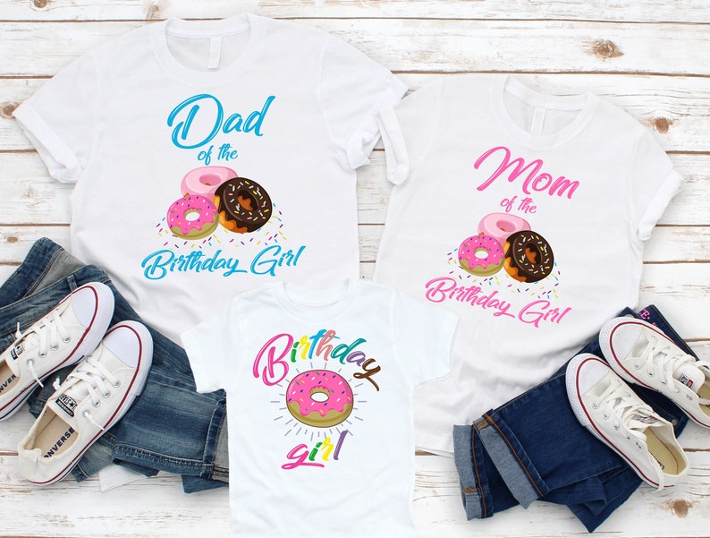 May include: Three white t-shirts with a donut theme. The shirts say "Dad of the Birthday Girl", "Mom of the Birthday Girl", and "Birthday Girl".