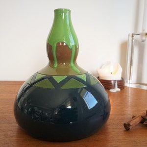 May include: A dark blue ceramic vase with a green and brown glaze. The vase has a rounded body and a narrow neck. The glaze has a drip effect, creating a unique and artistic look.