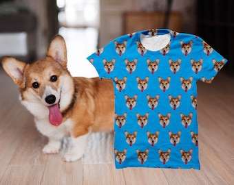 May include: A light blue t-shirt featuring a repeating pattern of a corgi's face. The corgi has brown and white fur, with its tongue sticking out. A live corgi dog is standing next to the shirt.