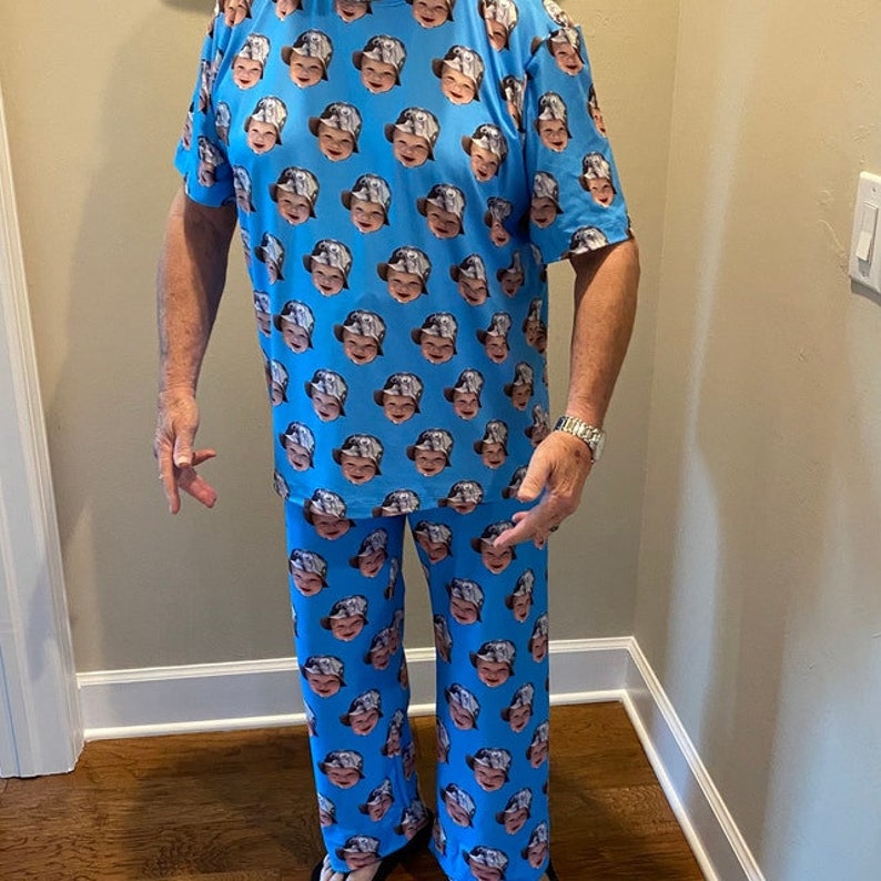 Op de afbeelding: Een blauwe pyjamaset met een herhalend patroon van een gezicht. Het pyjama-top heeft korte mouwen en de pyjamabroek heeft een rechte pijp.