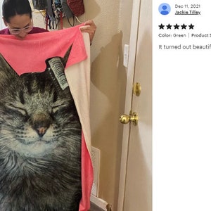 May include: A large, rectangular green and pink blanket featuring a close-up image of a cat's face. The blanket measures 50 x 60 inches. The cat has closed eyes and a serene expression.