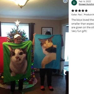 May include: Three fleece blankets, each featuring a large cat portrait. The blankets are held up by people, showcasing the cat images against red, green, and blue backgrounds. Each blanket measures 30" x 40".