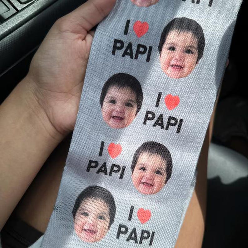Pu&ograve; includere: Tessuto grigio chiaro con la scritta "I ❤️ PAPI" e un motivo ripetuto di un volto di bambino. Simboli di cuore rosso sostituiscono la parola "love".