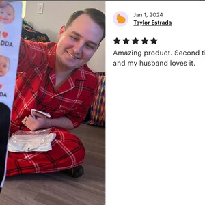 Pu&ograve; includere: Un paio di calzini bianchi e neri con la scritta "I DADDA" e foto di bambini. I calzini sono tenuti da una persona che indossa un pigiama a quadri rossi.