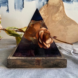Pyramid lamp made of epoxy resin, flowers and led light on a wooden base.