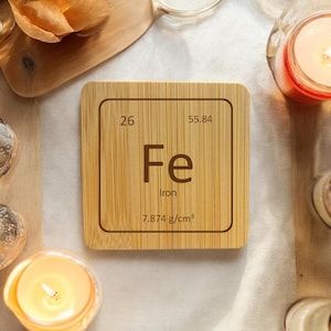 May include: A wooden coaster with the periodic table element for iron. The coaster is brown and has the atomic number 26, the symbol Fe, the name Iron, and the atomic weight 55.84. The density of iron is 7.874 g/cm3.