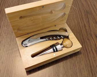 Puede incluir: Una caja de madera con un sacacorchos y un tapón de botella. El sacacorchos tiene un mango de madera y una espiral de metal plateado. El tapón de botella está hecho de madera y metal.