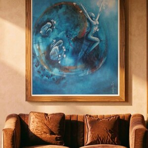 May include: A framed wall art piece featuring a blue circular composition with a central figure reaching upward, surrounded by smaller organic shapes and white floral accents, all enclosed in a simple wooden frame.