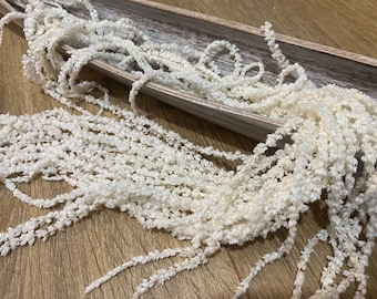 May include: A bunch of white dried flowers, also known as bunny tails, in a wooden tray. The flowers are soft and fluffy, and they are perfect for adding a touch of whimsy to any decor.