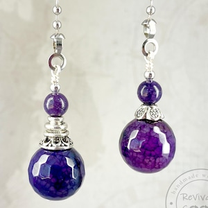 May include: Two purple agate crystal light pull chains with silver accents. The chains are made with a silver metal bead and a silver metal cap. The chains are handmade with heart by Revivabe Goods.