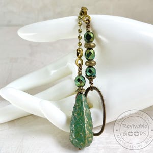May include: A ceiling fan pull chain featuring a brass ball chain, alternating green faceted glass beads, and textured brass spacers. The pull ends with a large, textured, teardrop-shaped green bead and a simple oval brass ring attachment.