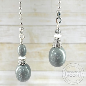 May include: Two gray and white beaded ceiling fan pull chains. Each chain has a silver-colored metal chain, a gray oval bead, a white bead, and a decorative silver-colored metal accent.