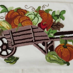 May include: A brown wooden wheelbarrow filled with pumpkins, gourds, and fall foliage. The wheelbarrow is decorated with brown and green yarn.