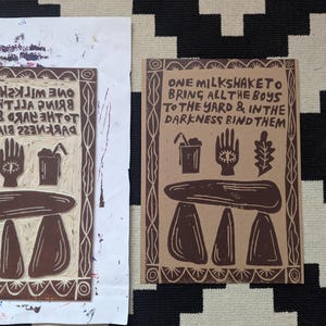 K&ouml;nnte beinhalten: Ein brauner Papierdruck mit dem Text "ONE MILKSHAKE TO BRING ALL THE BOYS TO THE YARD & IN THE DARKNESS BIND THEM". Der Druck zeigt eine Hand mit einem Auge, eine Tasse mit einem Strohhalm, ein Blatt und eine dreisteinige Struktur.