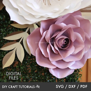 May include: A large, dusty rose paper flower with multiple layers of petals. The flower is surrounded by greenery and a smaller white paper flower.