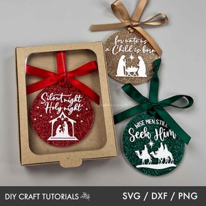 May include: Three round Christmas ornaments with glitter and white text. The ornaments are red, gold, and green. The red ornament says "Silent night Holy night" and features a nativity scene. The gold ornament says "for unto us a Child is born" and also features a nativity scene. The green ornament says "Wise men still Seek Him" and features three wise men riding camels.