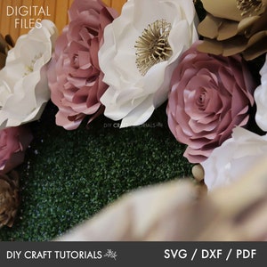 May include: A close-up of a paper flower wall backdrop with large white, pink, and gold paper flowers. The flowers are arranged in a circular pattern and are set against a green backdrop. The text "DIY CRAFT TUTORIALS" is visible at the bottom of the image.