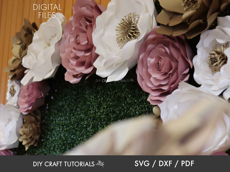 May include: A close-up of a paper flower wall backdrop with large white, pink, and gold paper flowers. The flowers are arranged in a circular pattern and are set against a green backdrop. The text "DIY CRAFT TUTORIALS" is visible at the bottom of the image.