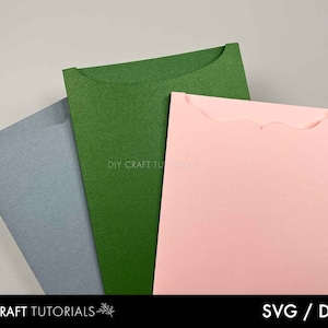 May include: Three colorful paper envelopes in shades of blue-grey, green, and pink. The green envelope has a curved top, while the pink envelope has a scalloped edge. The text "DIY CRAFT TUTORIALS" and "SVG / DXF" are visible.