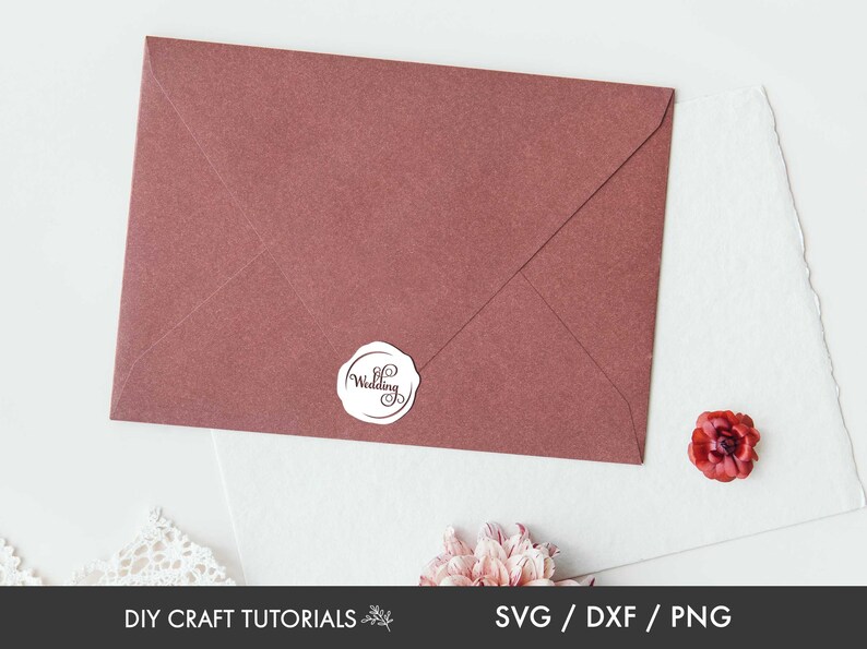 May include: A maroon envelope with a white round sticker that says "Wedding" in a cursive font. The envelope is on a white surface with a small red flower.