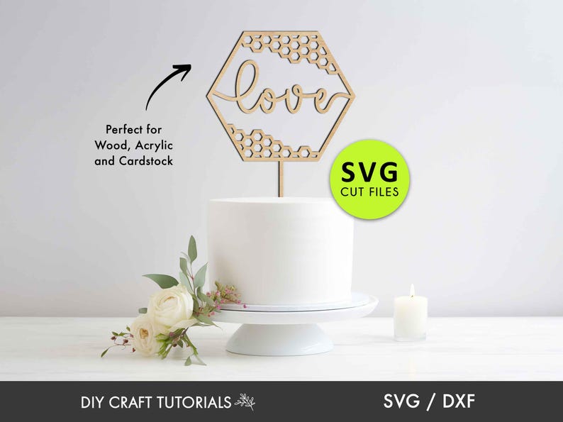 May include: A wooden hexagon cake topper with a honeycomb pattern and the word "love" in a cursive font. The topper is on a white cake stand with a white cake.