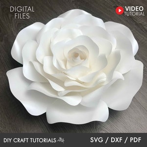 May include: A large white paper flower with multiple layers of petals. The flower is on a dark wood background. The text "DIY CRAFT TUTORIALS" and "SVG/DXF/PDF" are at the bottom of the image.