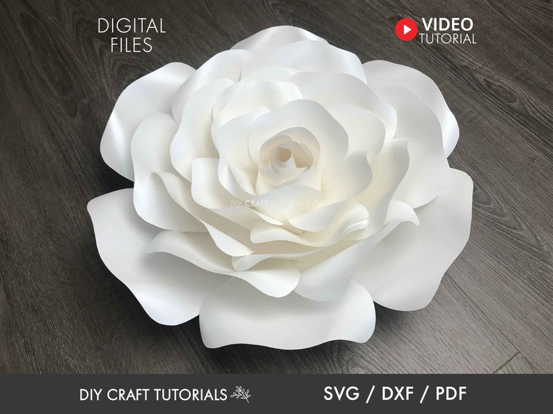 May include: A large white paper flower with multiple layers of petals. The flower is on a dark wood background. The text "DIY CRAFT TUTORIALS" and "SVG/DXF/PDF" are at the bottom of the image.