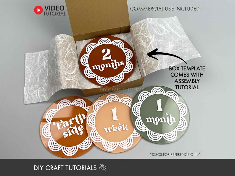 May include: Four round, decorative discs for a baby milestone photo prop. The discs are made of wood and have a white border with a decorative pattern. The discs feature the following text: "Earth side", "1 week", "1 month", and "2 months".