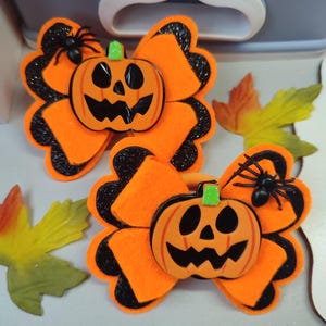 Può includere: Due fiocchi per capelli di Halloween arancioni e neri con una zucca di feltro e un ragno come ornamento.