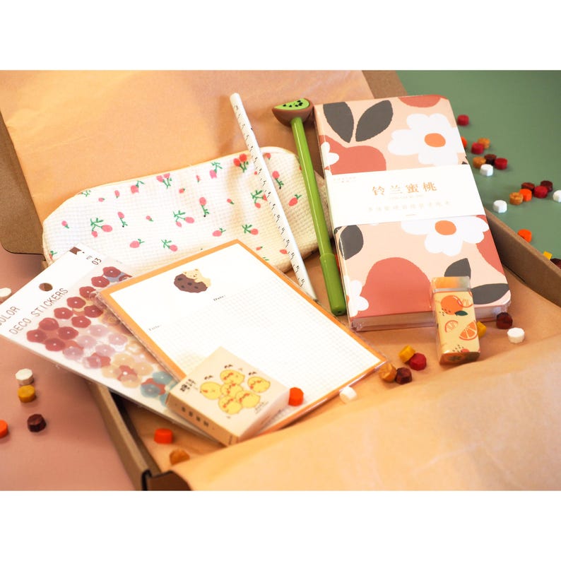 May include: A stationery set in a box, featuring a notebook with a floral design, a kiwi-shaped pen, stickers, notepaper, and a pencil case. The items have a pastel color palette with floral and fruit motifs.