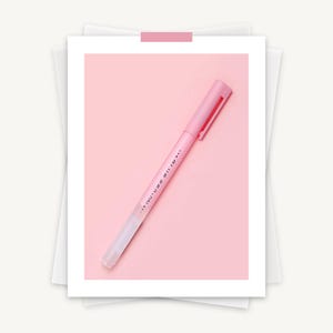 May include: A pink pen with a matching cap and clip, set against a pink background. The pen has text printed on the side. The pen is on a white background.
