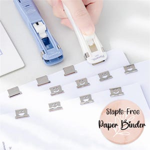 May include: Two blue and white plastic staple-free paper binders with the word "Planwith" printed on them. The binders are holding together a stack of white paper with silver smiley face paper clips.