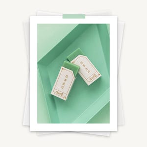 May include: Two green bars of soap with white labels that say "抹茶 生 巧" and "抹茶 生 巧" in Japanese. The soap is sitting on a light green tray.