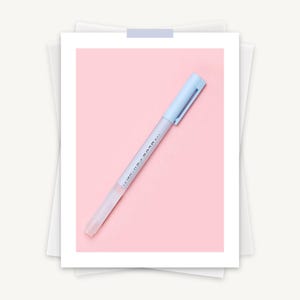 May include: A light blue pen with a matching cap and clip, set against a pink background. The pen's barrel is transparent, and the text "...BLUE PEN..." is printed on the side. The pen is resting on a white paper.