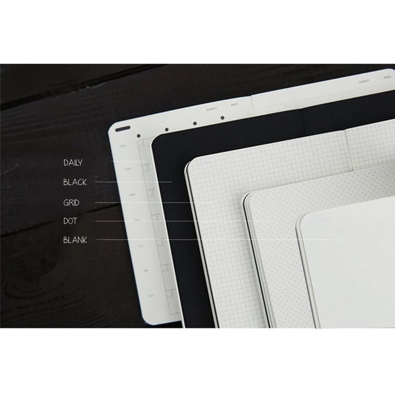 May include: Five different notebooks stacked on top of each other. The notebooks are all white with different patterns. The patterns are: daily, black, grid, dot, and blank.