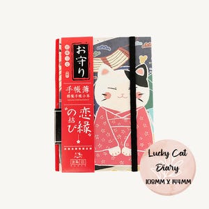 Può includere: Un diario in stile giapponese con un design a gatto fortunato. Il diario ha un dorso rosso con testo giapponese e una chiusura elastica nera. La copertina presenta un gatto in kimono e il testo "Lucky Cat Diary". Misura 10,8 cm x 14,4 cm.