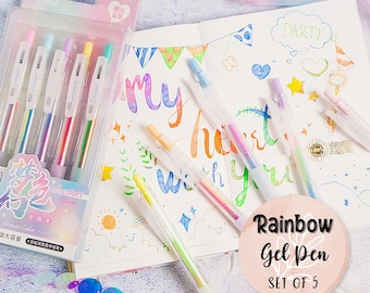 May include: Set of five rainbow gel pens in a clear plastic package. The pens are clear with rainbow colored ink. The pens are on a white surface with a notebook and a drawing of hearts and stars.