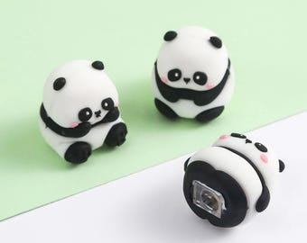 May include: Three small panda bear figurines. The pandas are white with black markings around their eyes, ears, and limbs. One panda is lying on its back, revealing a small light. The other two pandas are upright, with one in a sitting position.