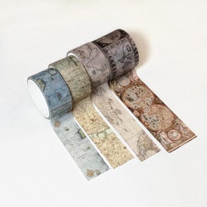 May include: Four rolls of adhesive tape featuring vintage-style cartographic designs. Each roll displays different historical map patterns in muted tones of blue, beige, grey, and sepia, including illustrations of compass roses and nautical grids.