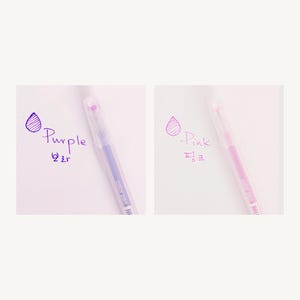 May include: Two clear gel pens with purple and pink ink. The pens have a clear barrel and a silver cap. The ink color is shown next to each pen with a drop of ink and the word "Purple" or "Pink" written in the corresponding ink color.